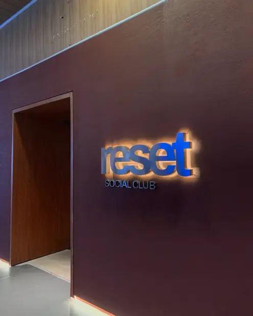 The illuminated blue reset social club sign on an oxblood wall